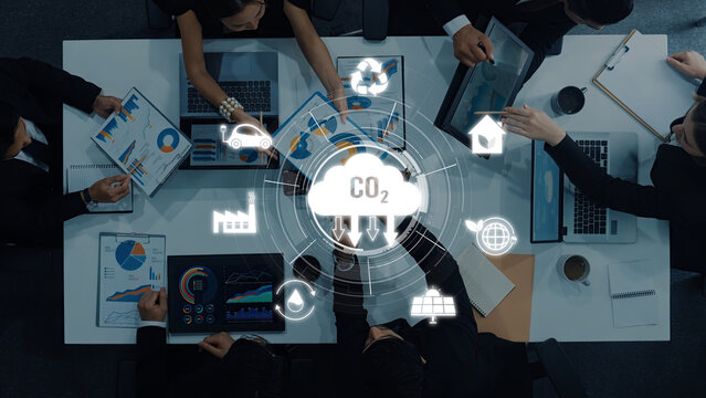 A diverse business team engages in a collaborative meeting focused on developing strategies to reduce carbon emissions. Modern office setting with technology and data. Trope