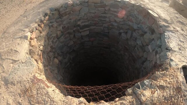 Close-up of an ancient dry-stone well structure with rusted mesh, set against a vast rocky desert and distant mountains under a bright sky &mdash; atmospheric B-roll for documentaries, archaeology projects.