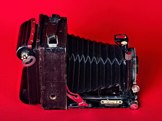 An old camera, with bellows, folding, portable on a red background:
