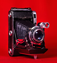 An old camera, with bellows, folding, portable on a red background: