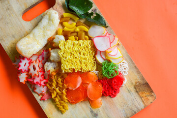 Crackers, cuanki, noodles, and complete dry seblak seasoning on a wooden tray