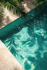 Clear turquoise swimming pool water with sunlight reflections and shadows of palm leaves on tiled poolside