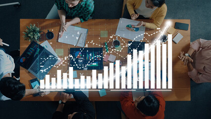 Aerial view of a team engaged in a collaborative meeting, analyzing data trends with graphs and charts displayed on laptops, enhancing productivity and communication. Axiom