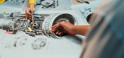 Engineers engage in a detailed analysis of mechanical components and technical drawings, showcasing collaboration and creativity in an innovative workshop setting. SACTR