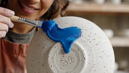 Woman artist painting white ceramic bowl with blue paint brush. Creative pottery decoration process in studio. Cinematic macro shot of artistic brush strokes and dripping paint on dishware. - Powered by Adobe