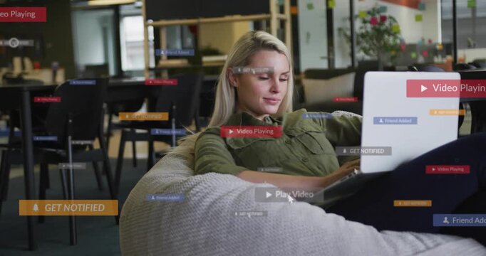 Woman sitting on beanbag in office typing on laptop starting animated alerts over lap for marketing
