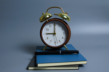 Naklejka premium Vintage alarm clock positioned centrally on top of notebook and pen against gray background, showing time management and daily routine concept.