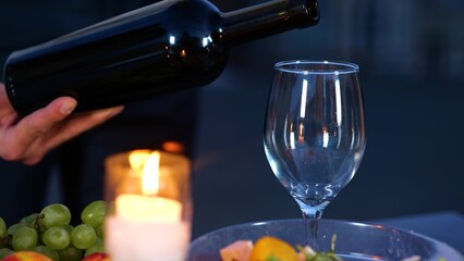 Close up of male hand holding a bottle of wine serving drink at a romantic date in evening. Man hand pouring luxury expensive red wine into glass outdoors. Romantic dinner outdoor
