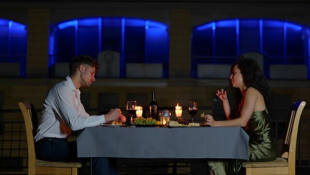 Camera approaching happy elegant couple sitting at decorated table with candles outdoor eating on romantic date. Anniversary celebration. Slow motion. Romantic date. Family concept