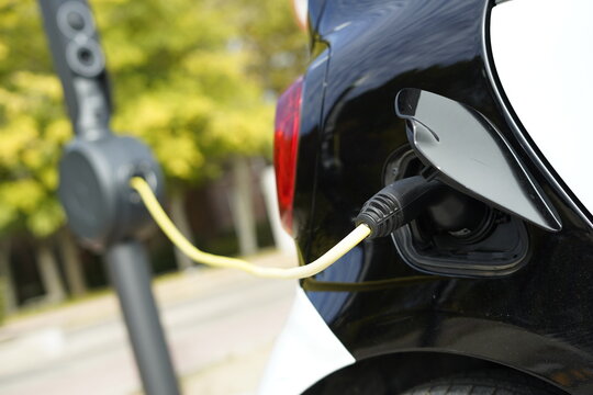 Detalle de un coche el&eacute;ctrico con el puerto de carga y enchufe conectado con cable para la carga de bater&iacute;a en la calle en una estaci&oacute;n de carga