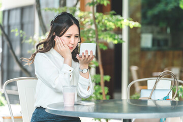 Fototapeta premium Young woman applying makeup in a cafe, looking in the mirror (moisturizing, UV protection, UV protection) 