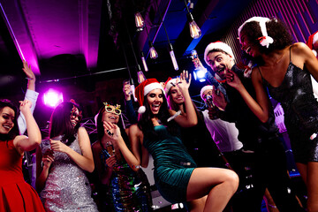 Energetic festive party scene with friends dancing in a nightclub wearing Santa hats and glamorous outfits as bright neon lights glow