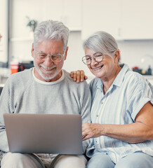 Pretty elderly 70s grey-haired couple resting on couch in living room hold on lap laptop watching movie smiling enjoy free time, older generation and modern wireless technology advanced users concept