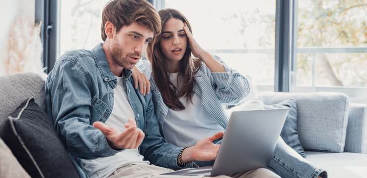 Millennial couple annoyed by stuck laptop or online news sitting together on sofa, frustrated young angry customers confused by computer problem feeling perplexed or puzzled about email message