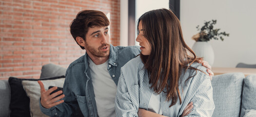 Beautiful lady is depressed, sitting on the couch talking to man, having a dispute with husband or boyfriend, looking desperate and hopeless, having unresolved problem or question