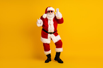 Santa in a festive red suit with white trim waves at the camera against a bright yellow background