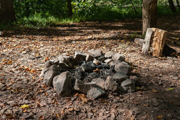 Campfire ring of rocks holds ash and coal from previous use at a wooden campsite