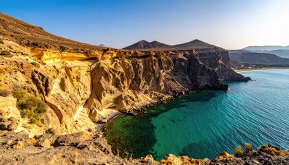 Rocky cliff face overlooking a clear turquoise lagoon and distant coastline under a bright blue sky