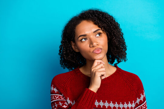 Funny thoughtful young woman in red sweater poses against blue background imagining christmas season and holiday magic