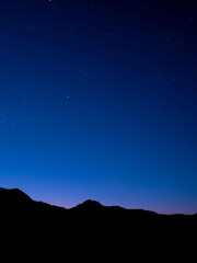 Deep blue night sky gradient over dark mountain silhouettes, scattered stars,  mountain range,  serene