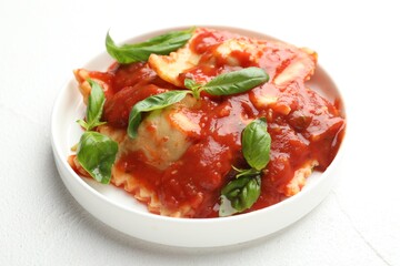 Delicious ravioli with tomato sauce and basil on white textured table, closeup