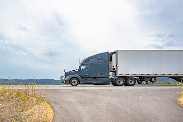 Gray bonnet big rig semi truck transporting cargo in refrigerated semi trailer driving on the highway road with fork intersection