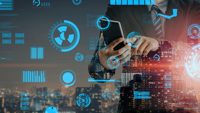 A businessman interacts with a smartphone while analyzing data visualized on a cityscape background at night, showcasing modern technology and analytics. Xenic