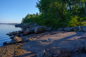 Rocky shoreline with forest and calm water on a clear summer morning
