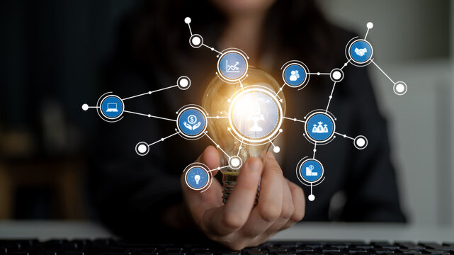 A conceptual image featuring a light bulb in hand, surrounded by various digital icons that represent innovation and technology in a modern business setting. Tessel - Powered by Adobe