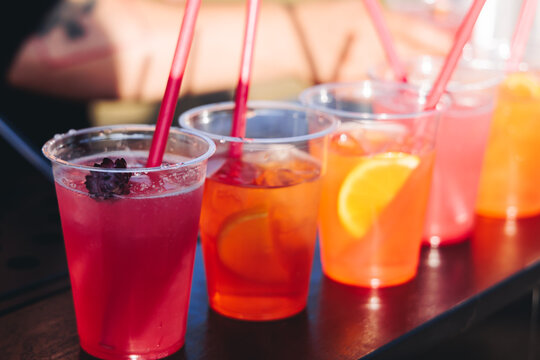 Barman mixing liquor beverages and alcohol drinks in plastic cups, bartender working, beautiful row line of different coloured cocktails on open air summer party in a bar, catering on banquet event