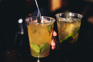 Barman mixing liquor beverages and alcohol drinks in plastic cups, bartender working, beautiful row line of different coloured cocktails on open air summer party in a bar, catering on banquet event