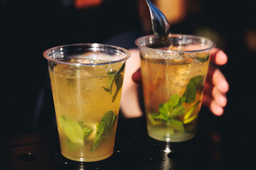 Barman mixing liquor beverages and alcohol drinks in plastic cups, bartender working, beautiful row line of different coloured cocktails on open air summer party in a bar, catering on banquet event