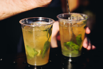 Barman mixing liquor beverages and alcohol drinks in plastic cups, bartender working, beautiful row line of different coloured cocktails on open air summer party in a bar, catering on banquet event