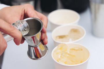 Barman mixing liquor beverages and alcohol drinks in plastic cups, bartender working, beautiful row line of different coloured cocktails on open air summer party in a bar, catering on banquet event