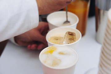 Barman mixing liquor beverages and alcohol drinks in plastic cups, bartender working, beautiful row line of different coloured cocktails on open air summer party in a bar, catering on banquet event