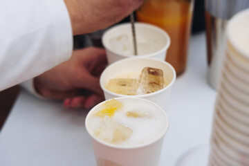 Barman mixing liquor beverages and alcohol drinks in plastic cups, bartender working, beautiful row line of different coloured cocktails on open air summer party in a bar, catering on banquet event