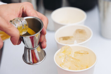 Barman mixing liquor beverages and alcohol drinks in plastic cups, bartender working, beautiful row line of different coloured cocktails on open air summer party in a bar, catering on banquet event