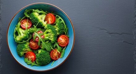 Fresh broccoli and cherry tomato salad in a blue bowl. A vibrant bowl of broccoli and tomato salad with arugula on a dark background