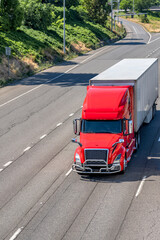 Red bonnet big rig semi truck with high roof transporting cargo in dry van semi trailer running on the road with fork intersection