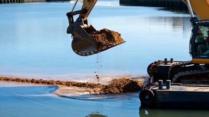Close medium shot of a backhoe dredger scooping sediment from the harbor floor maintaining navigable channel depth amid calm waters.