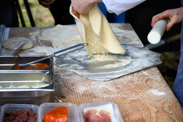 Chef rolling out raw pizza dough on wood table in preparation for cooking a wood fired pizza in a food truck outdoors in the fall
