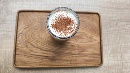A glass of traditional teh tarik (pulled tea) with a distinctive layer of foam, served at a restaurant table in the evening. This warm beverage is popular in Southeast Asian eateries.