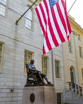John Harvard statue underneath US flag,  in front of University Hall in Old Harvard Yard, Harvard University, Cambridge, Massachusetts MA, USA