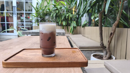 A glass of traditional teh tarik (pulled tea) with a distinctive layer of foam, served at a restaurant table in the evening. This warm beverage is popular in Southeast Asian eateries.