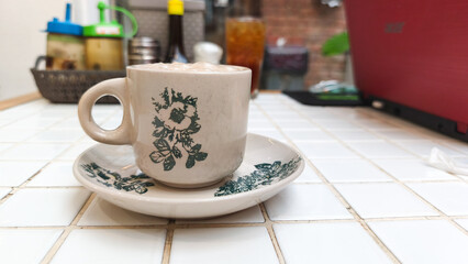 A glass of traditional teh tarik (pulled tea) with a distinctive layer of foam, served at a restaurant table in the evening. This warm beverage is popular in Southeast Asian eateries.