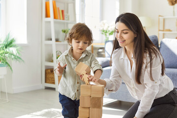 Mother and child play with blocks daily. In home, a parent helps a toddler kid stack wooden cubes,...