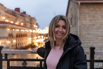 Woman portrait evening standing smiling happily in illuminated urban street with string lights background at twilight
