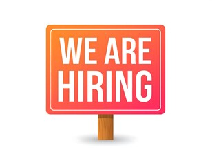 Bright orange sign reading "We Are Hiring" in white letters stands on wooden post