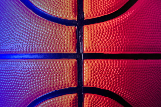 Detailed basketball, showcasing its textured surface and black seams under vibrant neon lighting