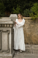 full length portrait of beautiful blonde female model wearing historical white gothic wedding gown, walking down staircase of romantic fairytale castle location with stone balconies